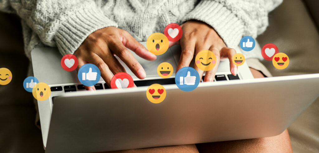 Person typing on a laptop with social media icons floating above it.